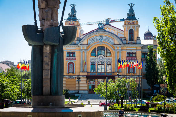 Cluj Napoca, Romania - 3 May, 2018: color image depicting one of the main public squares in Cluj Napoca, the largest city in the Transylvania region of Romania. There is a large statue in the middle of the square, while beyond this lies the impressive architecture of the national theatre and opera house. Image taken on a warm summer day with blue sky. Room for copy space.