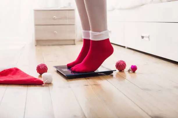 Photo of Female feet standing on electronic scales for weight control in red socks with Christmas decoration