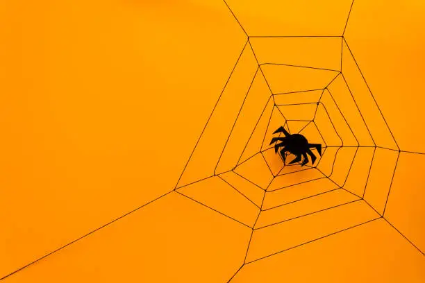 Photo of Black paper spider with web on yellow background. Halloween concept. Paper cut style. Top view