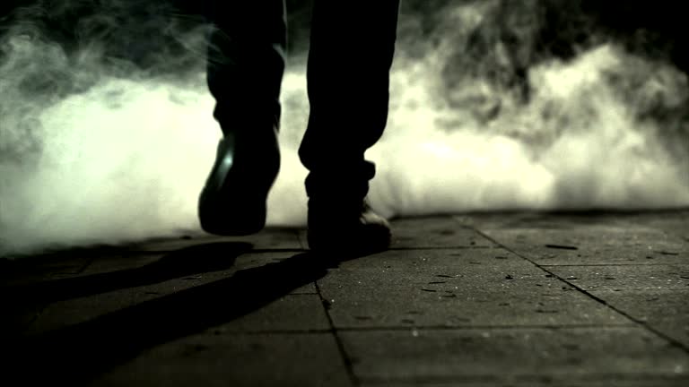 The legs of a man walking near the cloud of a smoke. slow motion