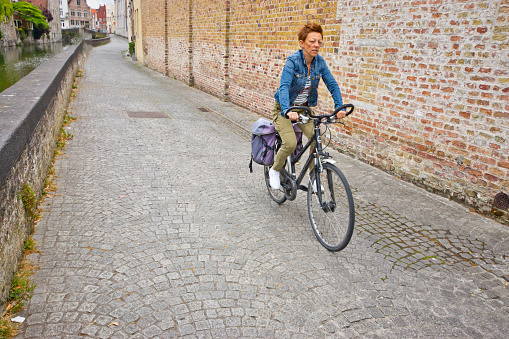 Woman cycling through Bruges over the cobblestones near the canal.