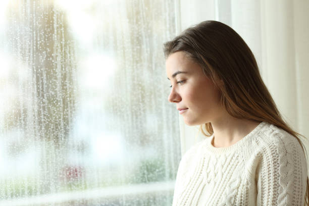 istock Sad woman looking through a window a rainy day 1030849970