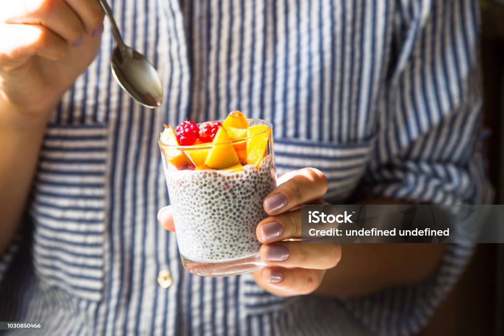 Chia pudding on coconut milk with raspberries and peach in a glass jar in female hands with a spoon. Raw vegan healthy food concept Chia seed Stock Photo