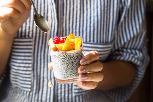 chia pudding na mleku kokosowym z malinami i brzoskwinią w szklanym słoiku w żeńskich rękach łyżką. surowa wegańska koncepcja zdrowej żywności - yogurt jar cream milk zdjęcia i obrazy z banku zdjęć