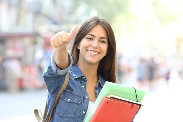 estudiante feliz posando con los pulgares para arriba en la calle - college girl fotografías e imágenes de stock