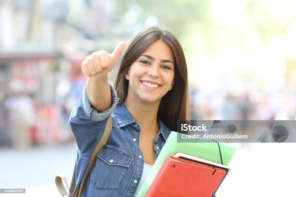 Happy student posing with thumbs up in the street Happy student posing with thumbs up looking at you in the street Student Stock Photo