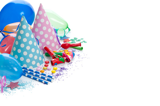 Party or carnival backgrounds. High angle view of multi colored accessories like balloons, party hats, party horn blowers, confetti, candies and streamers shot at the top-left corner of white background leaving useful copy space for text and/or logo. High key DSRL studio photo taken with Canon EOS 5D Mk II and Canon EF 100mm f/2.8L Macro IS USM.