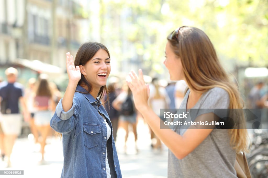 Friends meeting and greeting in the street Two happy friends meeting and greeting in the street Greeting Stock Photo