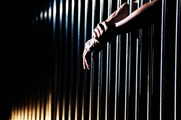 istock close up of prisoner hands in jail. 1030874678