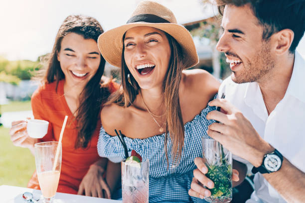 Friends drinking cocktails and laughing Small group of young people drinking cocktails and talking in the summer holiday camp stock pictures, royalty-free photos & images