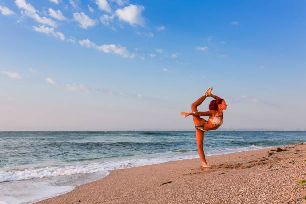istock Flexible Circus Performer, red-haired female acrobat practicing on the beach by the sea 1030897780