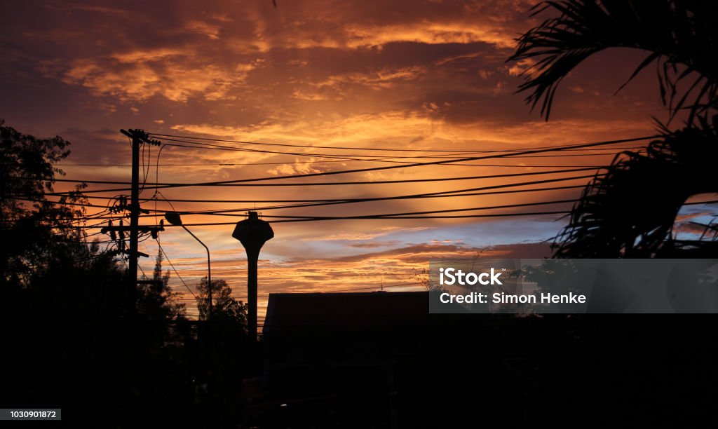 dramatic sky with silhouette of power lines in front Orange colored sky after sunset shows the silhouette of palms and houses of khao lak in thailand Black Color Stock Photo