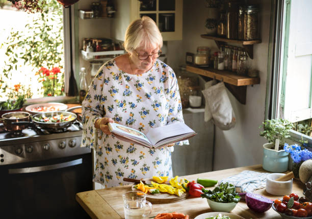 anciana leyendo un libro de cocina en la cocina - cookbook recipe book old fotografías e imágenes de stock