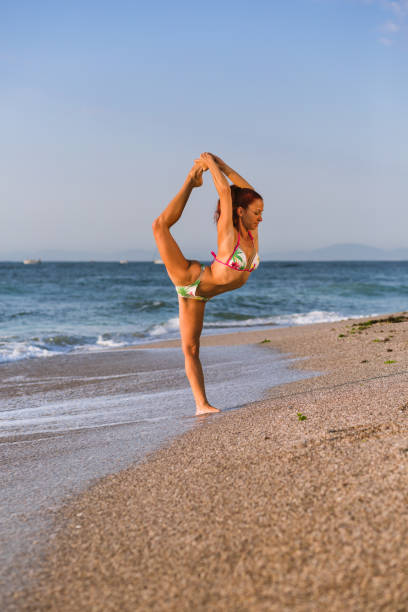 istock Flexible Circus Performer, red-haired female acrobat practicing on the beach by the sea 1030906690