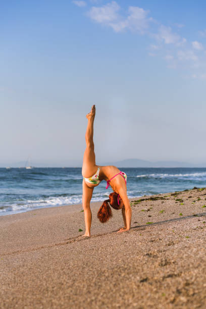 istock Flexible Circus Performer, red-haired female acrobat practicing on the beach by the sea 1030907068