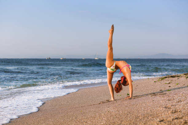 istock Flexible Circus Performer, red-haired female acrobat practicing on the beach by the sea 1030907692