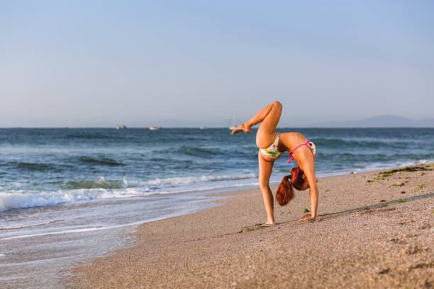 istock Flexible Circus Performer, red-haired female acrobat practicing on the beach by the sea 1030908332