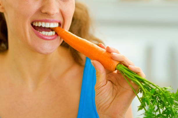istock Happy young woman eating carrot in kitchen 1030911396
