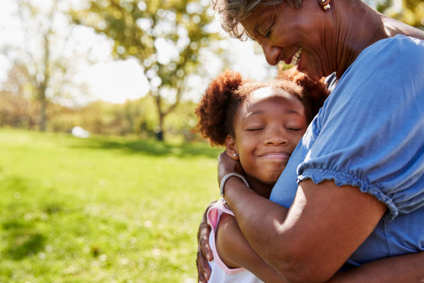 close up of granddaughter hugging grandmother in park - grandparent multi generation family family child imagens e fotografias de stock