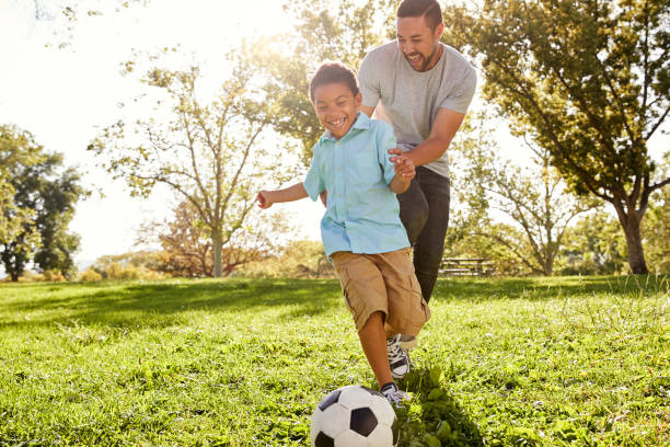 отец и сын играют в футбол в парке вместе - спортивная деятельность стоковые фото и изображения