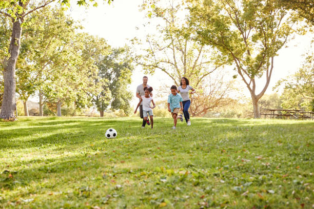 famiglia che gioca a calcio nel parco insieme - football player group of people running american football foto e immagini stock