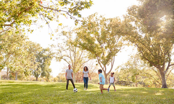 famiglia che gioca a calcio nel parco insieme - football player group of people running american football foto e immagini stock