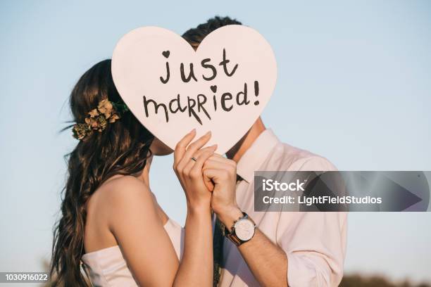 Young Wedding Couple Kissing And Holding Heart With Just Married Inscription Stock Photo - Download Image Now