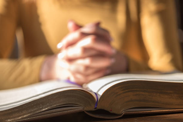 istock Woman praying with her hands over the bible, hard light 1030916962