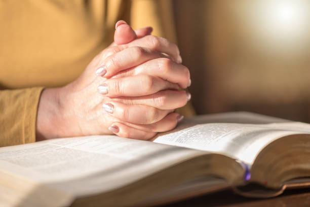 istock Woman praying with her hands over the bible, hard light 1030917036