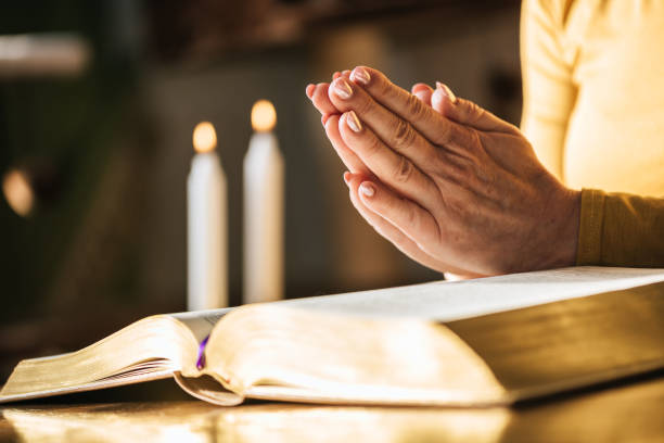 istock Woman praying with her hands over the bible, hard light 1030917900