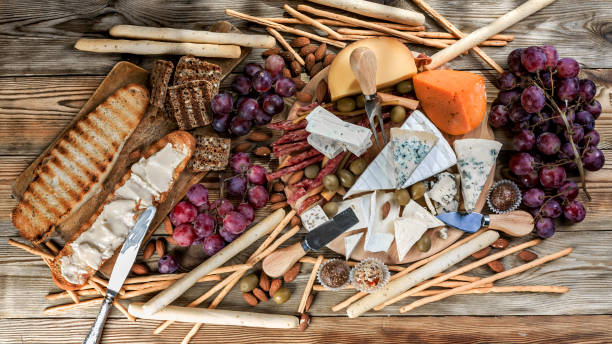 verschiedene arten von käse und trauben auf einem hölzernen hintergrund. - cheese emmental cheese swiss culture cutting board stock-fotos und bilder