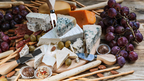 verschiedene arten von käse und trauben auf einem hölzernen hintergrund. close-up - cheese emmental cheese swiss culture cutting board stock-fotos und bilder