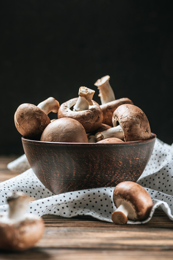 ripe champignon mushrooms in bowl on wooden table isolated on black