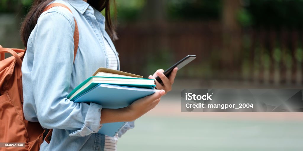 Chica estudiante con libros y smartphone mientras camina en el fondo del campus de escuela, educación, regresar al concepto de escuela - Foto de stock de Universidad libre de derechos