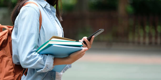 Student girl holding books and smartphone while walking in school campus background, education, back to school concept Student girl holding books and smartphone while walking in school campus background, education, back to school concept back to school teens stock pictures, royalty-free photos & images