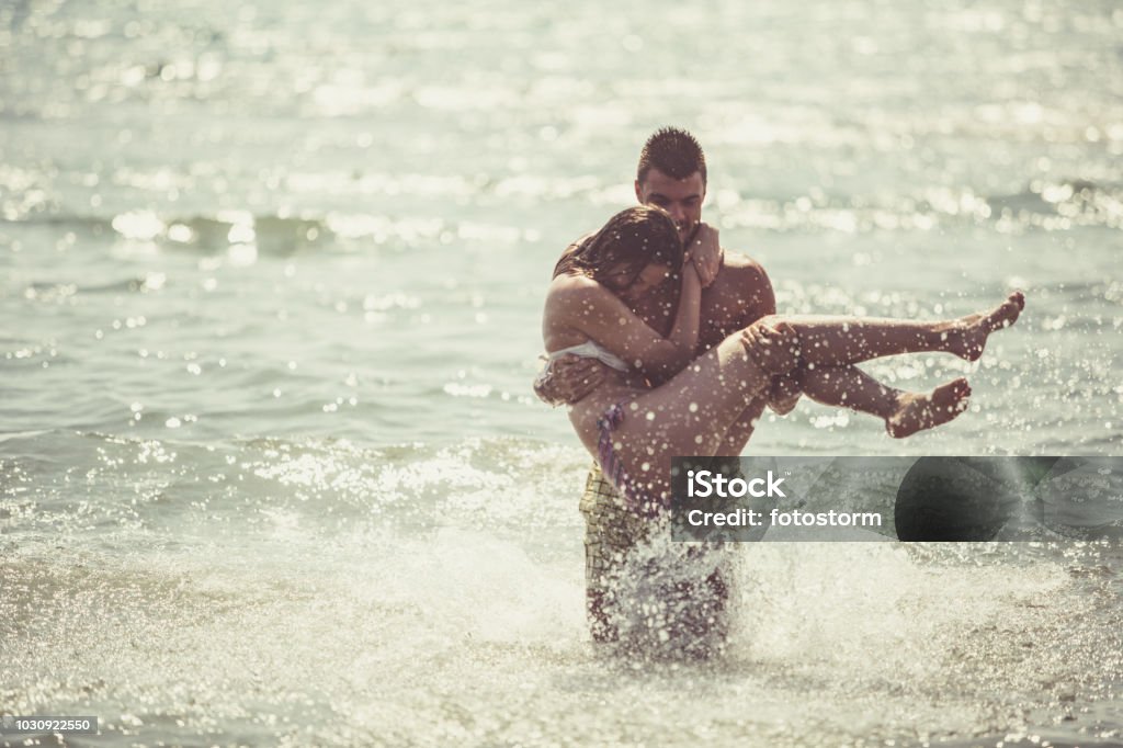 Romantic couple on a vacation A young man is carrying a woman in his arms in a shallow water. 18-19 Years Stock Photo