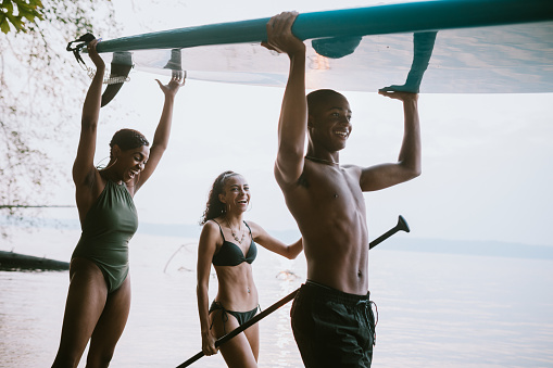 A group of teenagers play in and around the salt water of the Puget Sound, an inlet of the Pacific Ocean in Washington state, in the United States.  They carry their standup paddleboard to the waters edge.