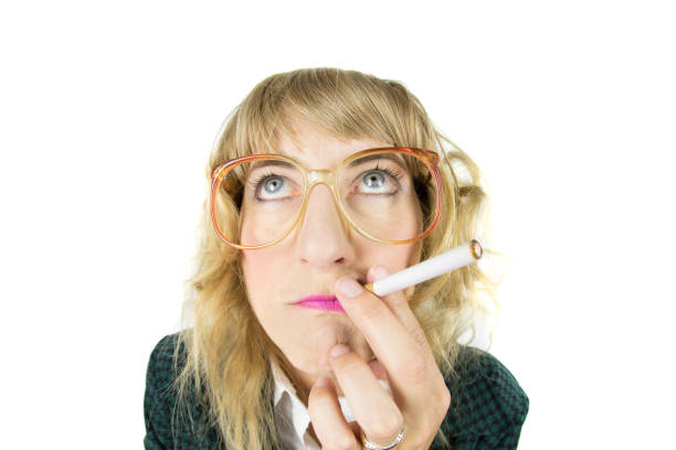 An older man, wearing glasses, smoking against a stone wall