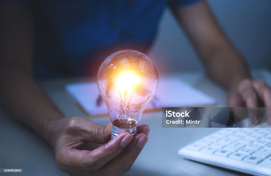 Business woman holding light bulb on the desk in office and using  computer in  financial,accounting,energy,idea concept. Resourceful Stock Photo