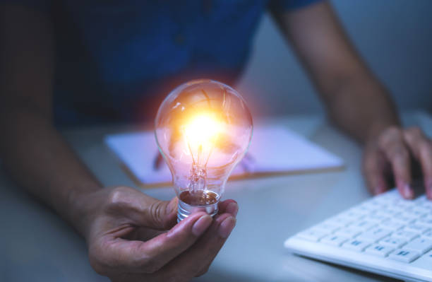 mulher de negócios, mantendo a lâmpada sobre a mesa no escritório e usando o computador em financeira, contabilidade, energia, conceito de ideia. - improvise - fotografias e filmes do acervo