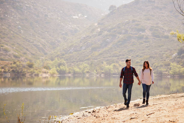 istock Young couple walk holding hands by a mountain lake 1030966132