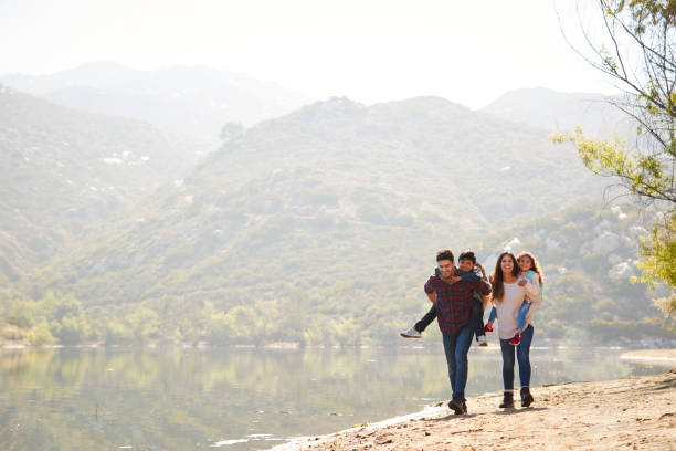 padres piggybacking sus hijos por un lago de montaña - family white family with two children cheerful fotografías e imágenes de stock