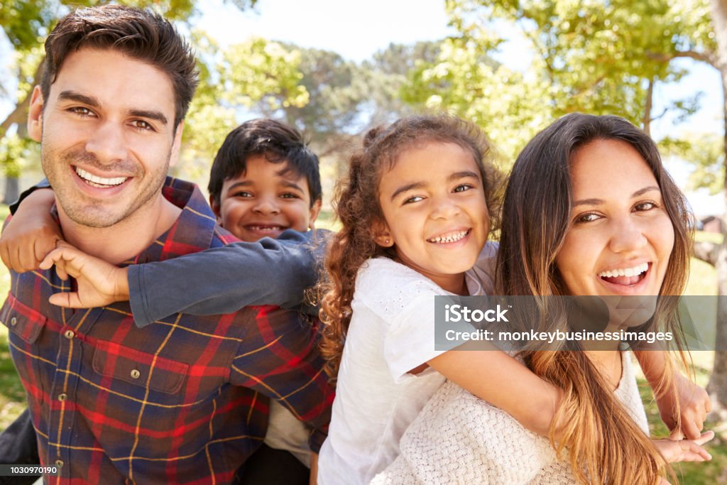 Young parents piggybacking their two kids outdoors Family Stock Photo