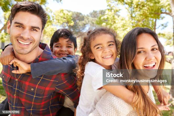 Young Parents Piggybacking Their Two Kids Outdoors Stock Photo - Download Image Now - Family, Multiracial Group, Happiness