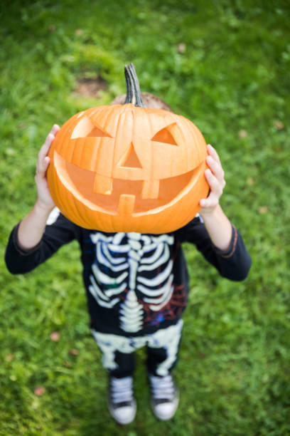 istock Boy in skeleton costume holding pupmkin 1030986374