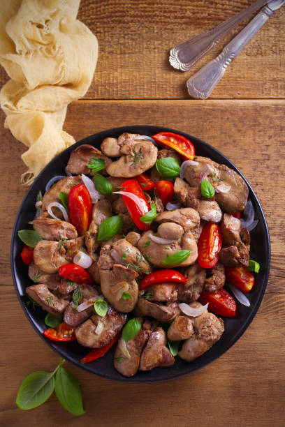 istock Chicken liver with  tomatoes, onions and basil on black plate, wooden table 1030992694