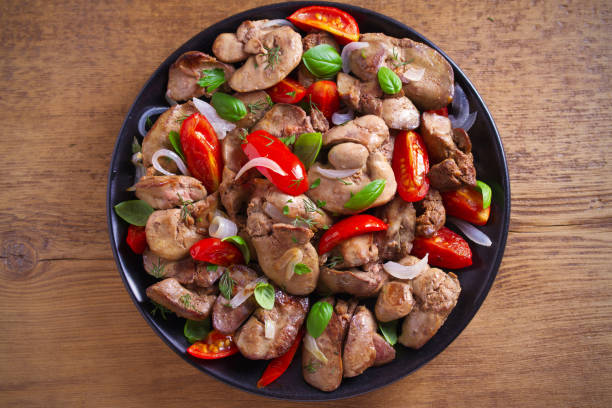 istock Chicken liver with  tomatoes, onions and basil on black plate, wooden table 1030992790