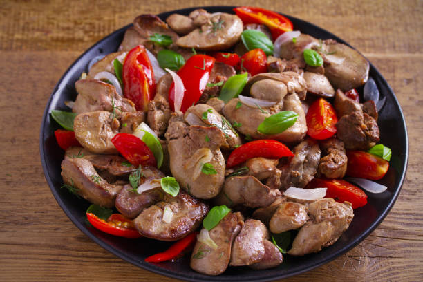 istock Chicken liver with  tomatoes, onions and basil on black plate, wooden table 1030992856