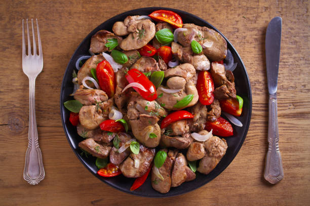 Chicken liver with  tomatoes, onions and basil on black plate, wooden table