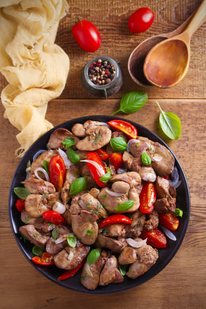 istock Chicken liver with  tomatoes, onions and basil on black plate, wooden table 1030995980